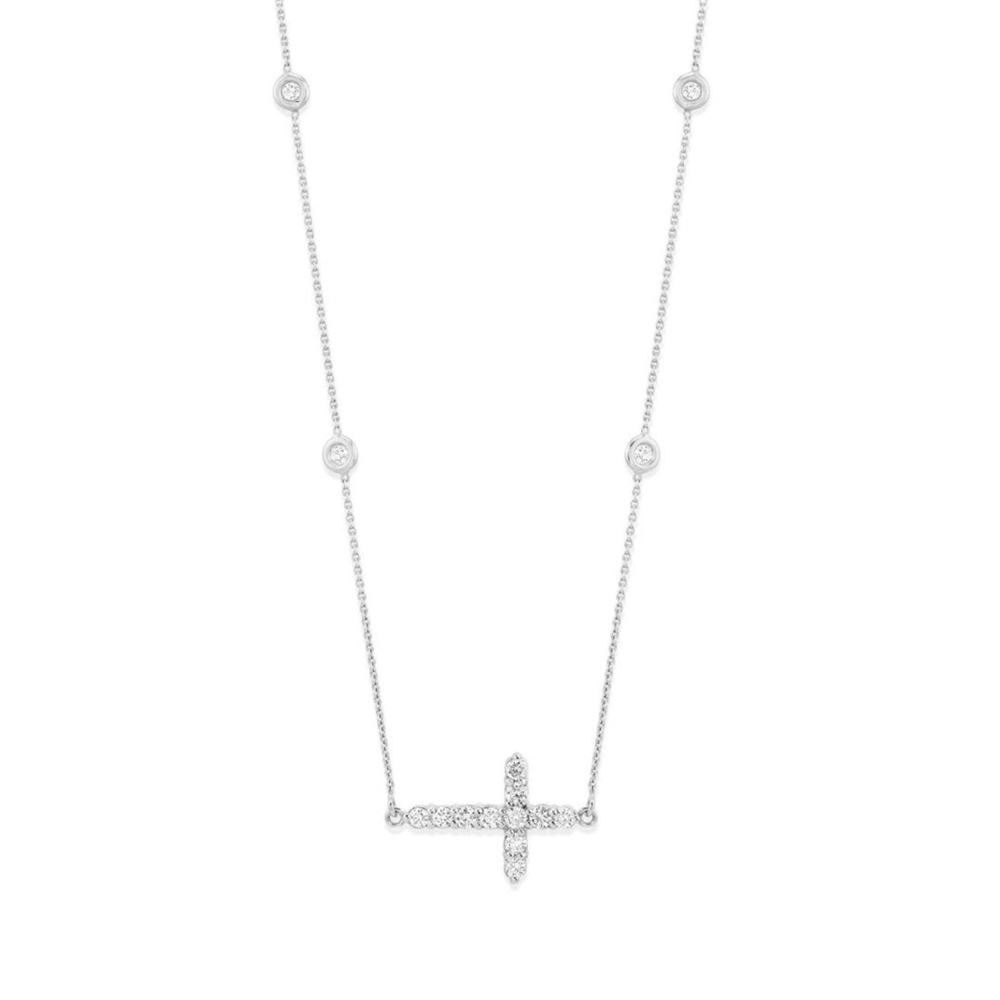 The Roberto Coin Tiny Treasures 18K White Gold Diamond Cross Necklace Pendant highlights an exquisite 18K white gold cross pendant adorned with small dazzling diamonds. The delicate chain is embellished with evenly spaced round diamond accents, enhancing the elegance of its minimalist design against a white backdrop.