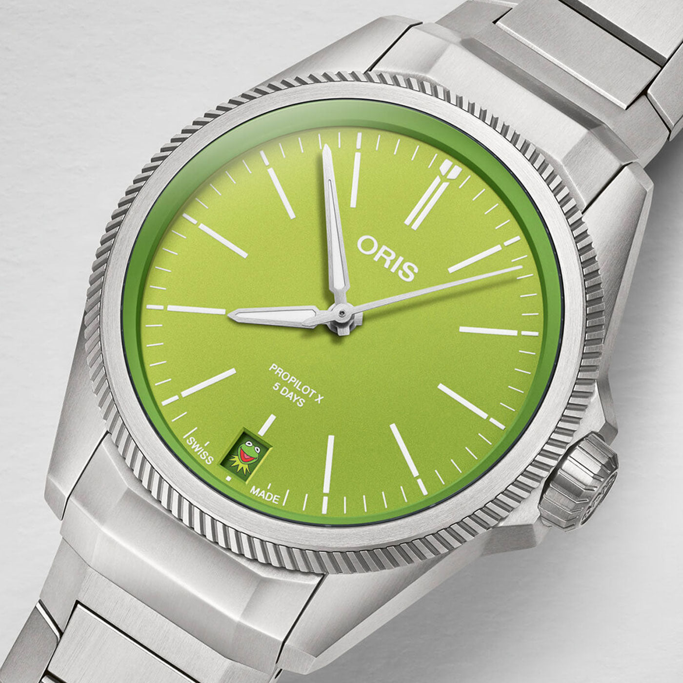 The Oris Propilot X Kermit Edition Automatic 39mm Watch is a silver wristwatch that showcases a bright green dial with silver hour markers and hands. The "ORIS" branding decorates the 12 o’clock position, while its minimalist design includes a date window and additional branding near the 6 o’clock mark on the dial.