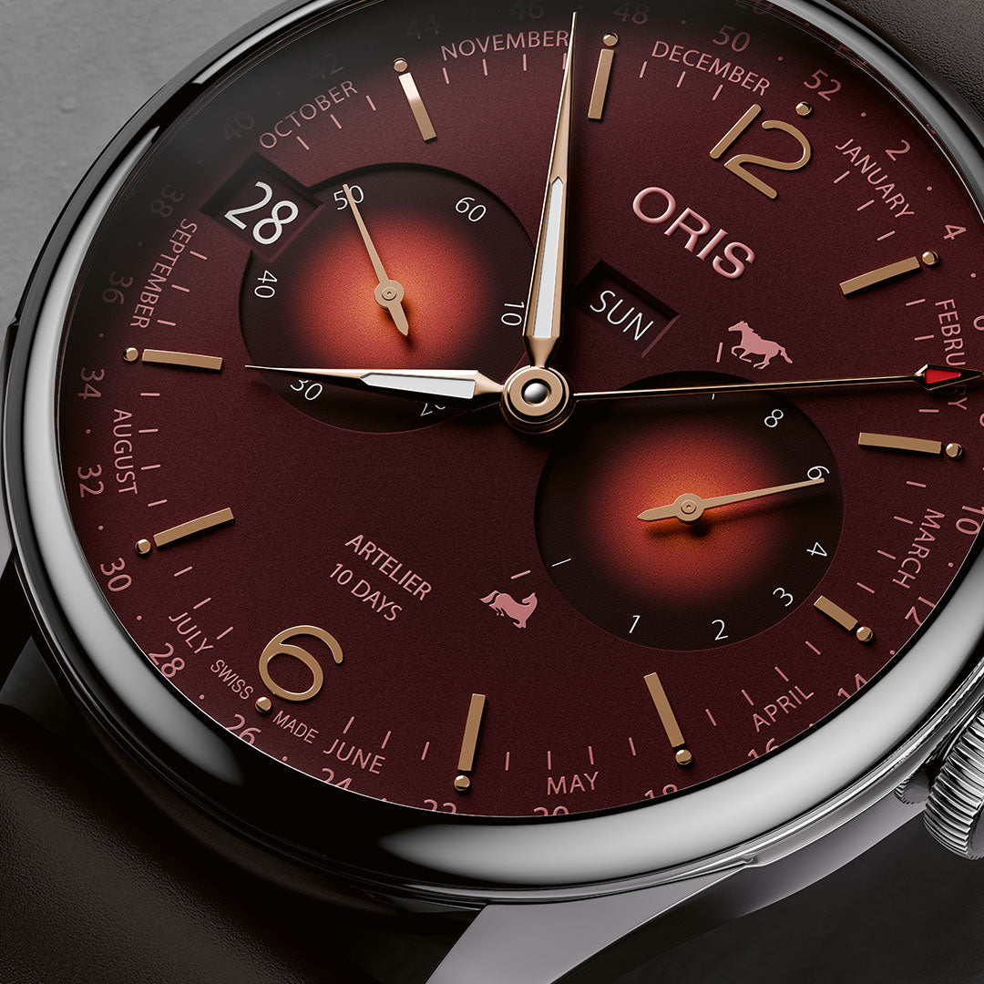 Close-up of the ORIS Artelier Year of the Horse Automatic 43mm Limited Edition watch (88 pieces) with a deep red dial, gold markers, subdials, calendar months, and brown leather strap. Features include date, day, and power reserve indicators.