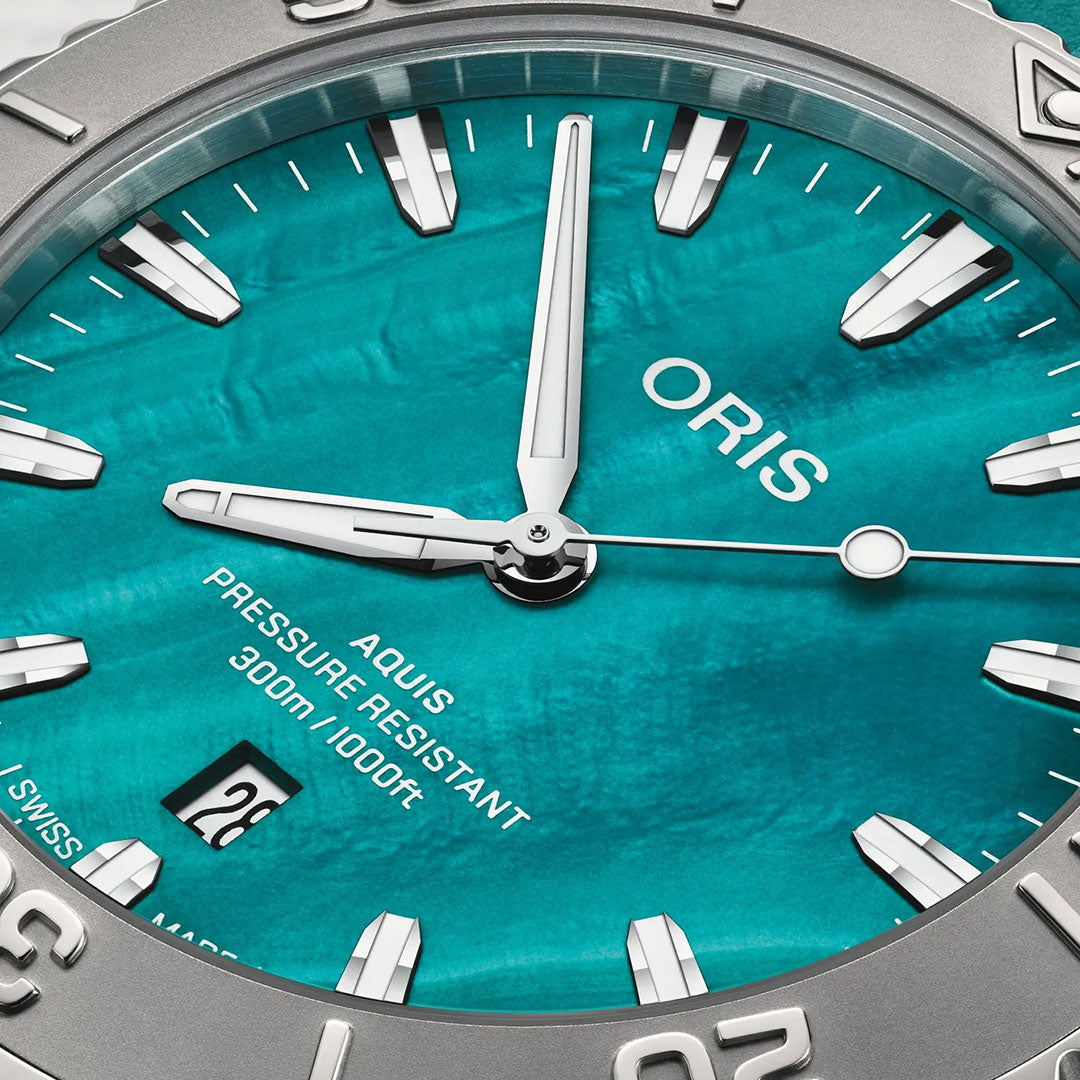 Close-up of the ORIS Aquis New York Harbor Limited Edition Automatic Winding 43.5mm Watch, showcasing a textured turquoise dial with silver markers and hands, date at 6 o’clock, "PRESSURE RESISTANT 300m/1000ft," and "SWISS MADE" inscription.