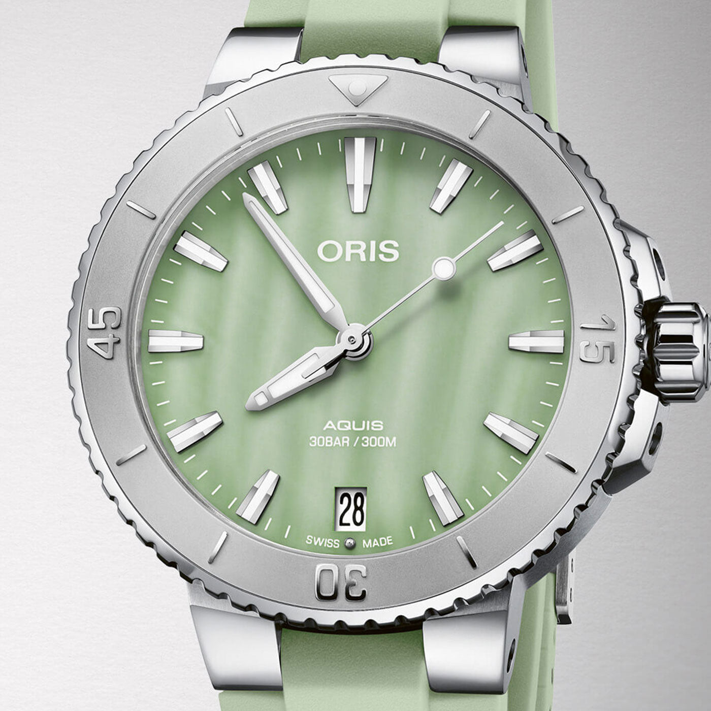 The ORIS Aquis Date Automatic Winding 36.5mm Watch is a stylish timepiece with a silver and green design, featuring a round face with three hands. Its vibrant green dial showcases white hour markers and includes a date display at the 6 o'clock position. The outer bezel has raised numerals, paired perfectly with the matching green strap, while the brand name "ORIS" is prominently displayed on the dial.