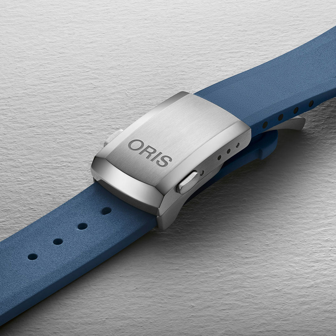 Close-up of a silver ORIS watch buckle attached to the blue strap of the Oris Aquis Date Automatic Winding 43.5mm Watch, set against a light textured background, showcasing its modern versatile classic appeal.
