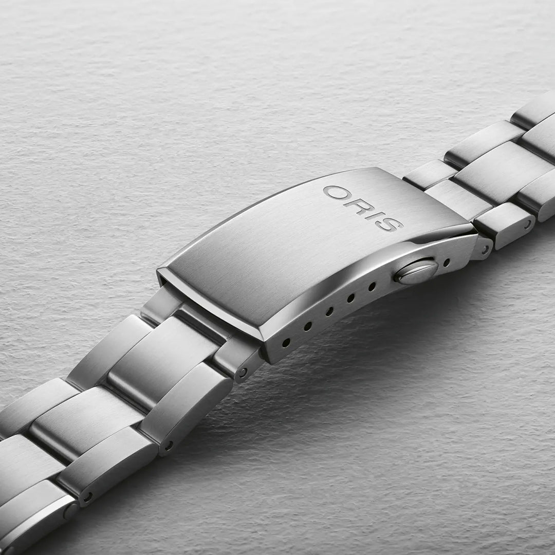 Close-up of an ORIS watch bracelet with an engraved clasp on a light gray surface. The polished links enhance the sophisticated design of the Oris Divers Date Automatic Winding 39mm Watch, featuring Swiss Made automatic movement and a durable ceramic bezel for lasting elegance.