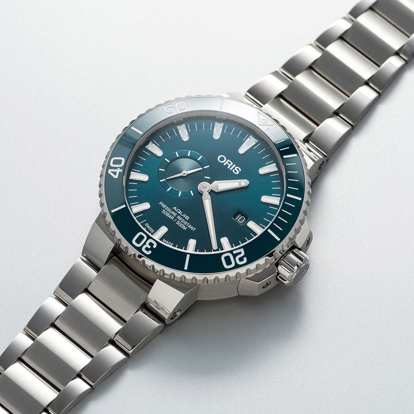 The Oris Aquis Small Second Date Automatic 45.5mm Watch by ORIS features a stainless steel construction, blue dial, and white hour markers. It includes a date window at the 3 o'clock position and a bezel with minute markings, all displayed on a light gray background.