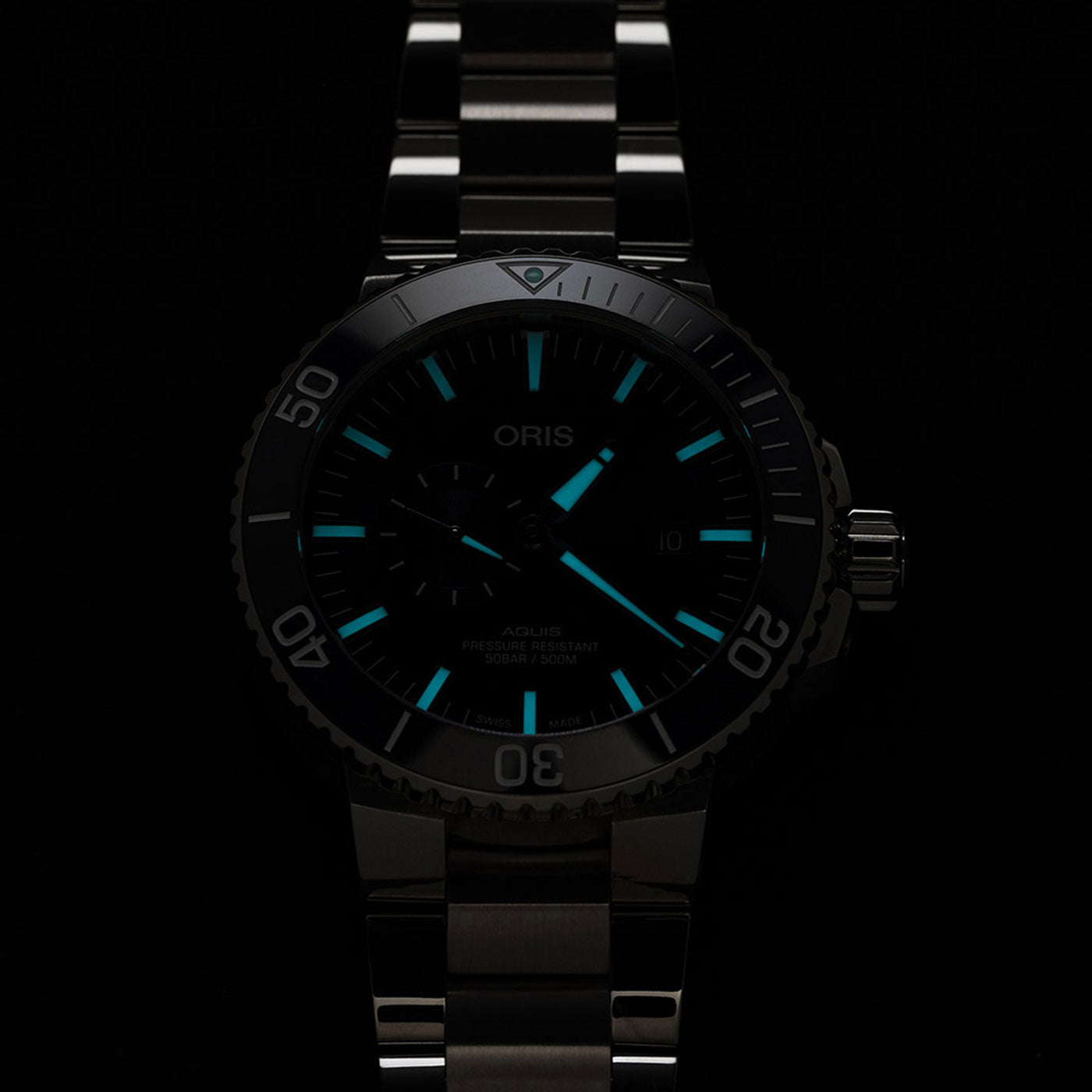 The Oris Aquis Small Second Date Automatic 45.5mm Watch by ORIS features a stainless steel design with glow-in-the-dark hour markers and hands, highlighted by luminous turquoise accents on a dark background.