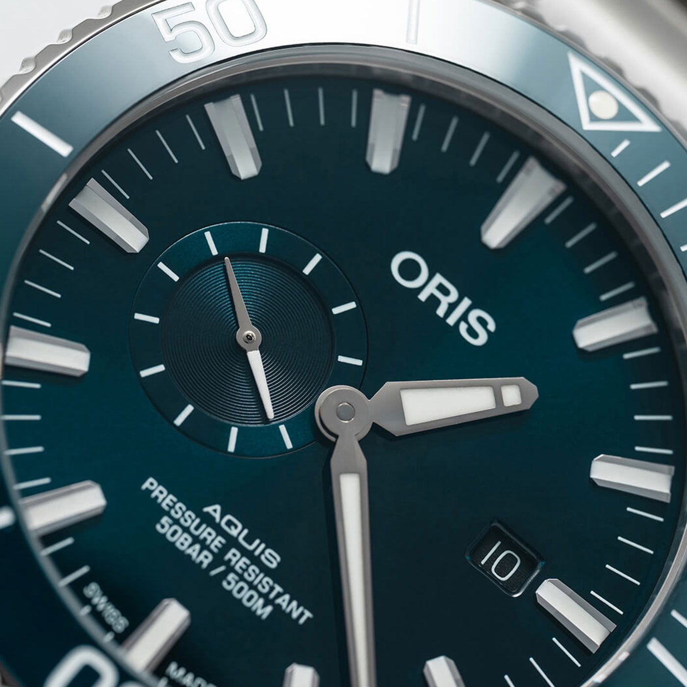 Close-up of the Oris Aquis Small Second Date Automatic 45.5mm watch face in blue, featuring white hour markers, a small seconds sub-dial, and a date window. The ORIS watch is pressure resistant up to 500 meters. The bezel is partially visible with a 50 mark.