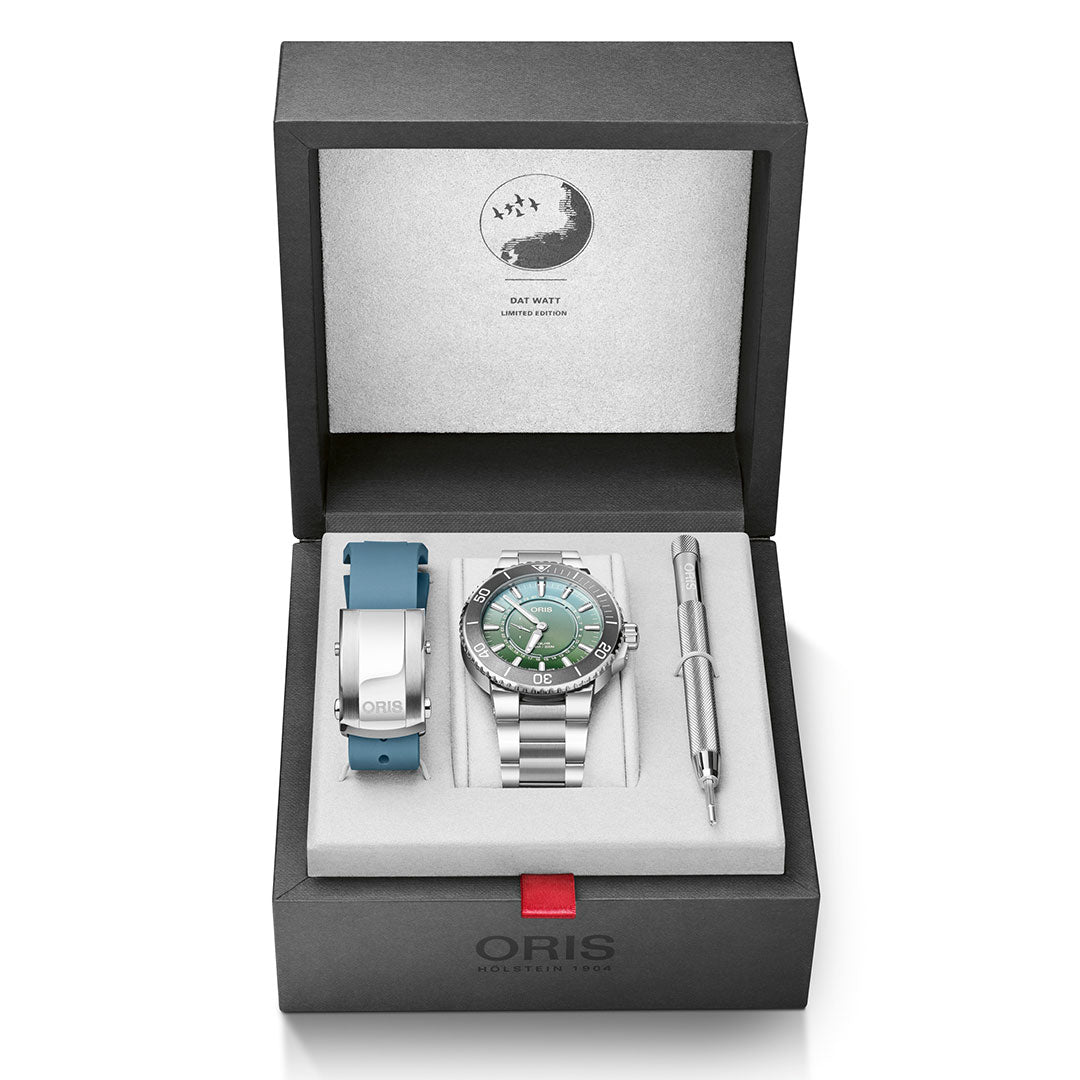 The Oris Aquis Dat Watt Limited Edition II Automatic Winding 43.5mm Watch by ORIS includes a luxury silver and green diver’s watch, accompanied by an interchangeable blue strap and a metal tool, all beautifully presented in a black box. The lid is adorned with a partial moon design featuring the words "Day Date.