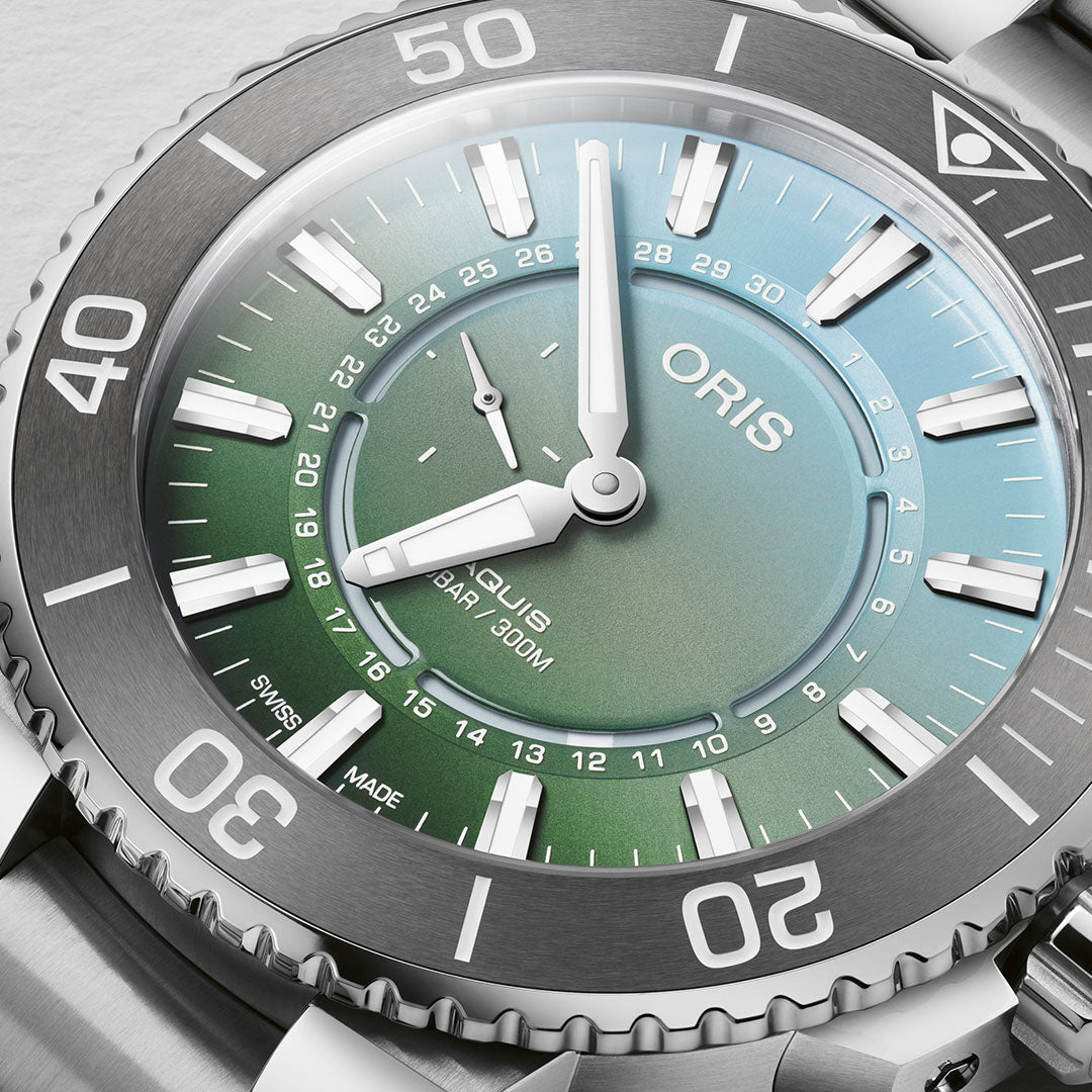Close-up of a silver Oris Aquis Dat Watt Limited Edition II Automatic Winding 43.5mm Watch by ORIS, featuring a gradient green and blue dial. The bezel is adorned with large numeric markings, and the prominent hands and hour markers highlight its sleek, modern design. This watch represents both style and a dedication to conservation.