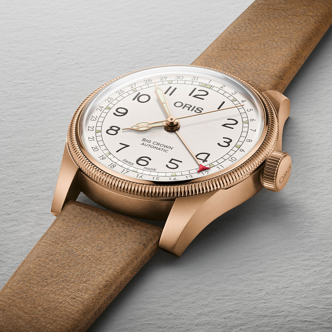 Introducing the Oris Big Crown Father Time Limited Edition Automatic Winding 40mm Watch, elegantly designed with a bronze case and tan leather strap. It features a cream dial with black Arabic numerals, an outer date ring, and a red-tipped pointer. The iconic "ORIS" branding graces both the dial and crown.