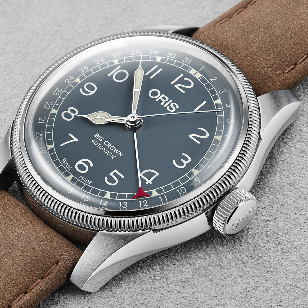 A close-up of an Oris Big Crown Pointer Date Automatic Winding 44mm Watch by ORIS showcases its oversized crown, black dial with white Arabic numerals, silver watch hands, and a distinct red-tipped seconds hand. The stainless steel case and brown leather strap are set against a grey background.