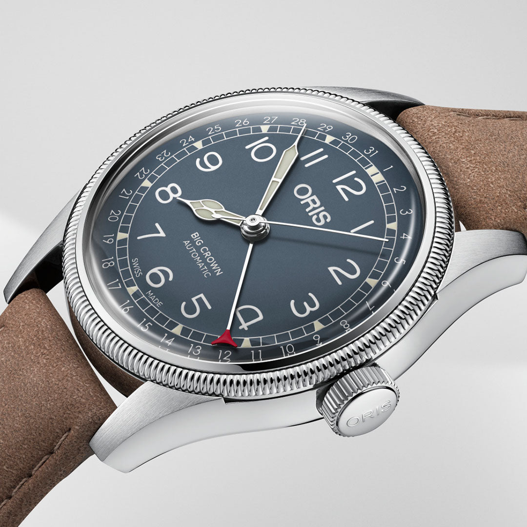 The Oris Big Crown Pointer Date Automatic Winding 44mm Watch by ORIS is crafted from silver, showcasing a striking blue dial with large white numerals. It is adorned with a brown leather strap and features an oversized crown on the side. The watch's design evokes the essence of classic pilot's watches and includes silver minute and hour hands, along with a distinctive red-tipped second hand.