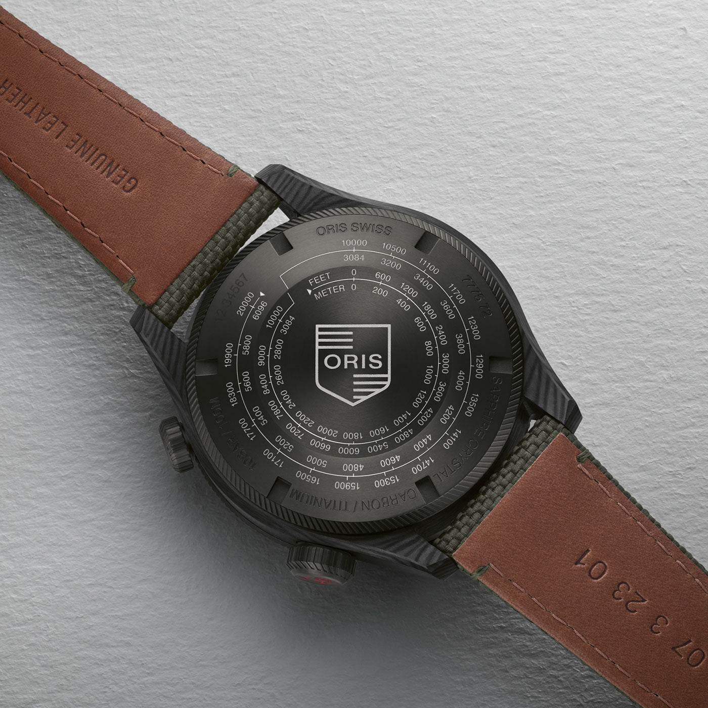 The Oris Propilot Altimeter Automatic 47mm Watch by ORIS features a black case with a textured back that displays various depth measurements along with the Oris logo. It comes with a brown leather strap embossed with the words "GENUINE LEATHER" and is showcased on a white textured surface.