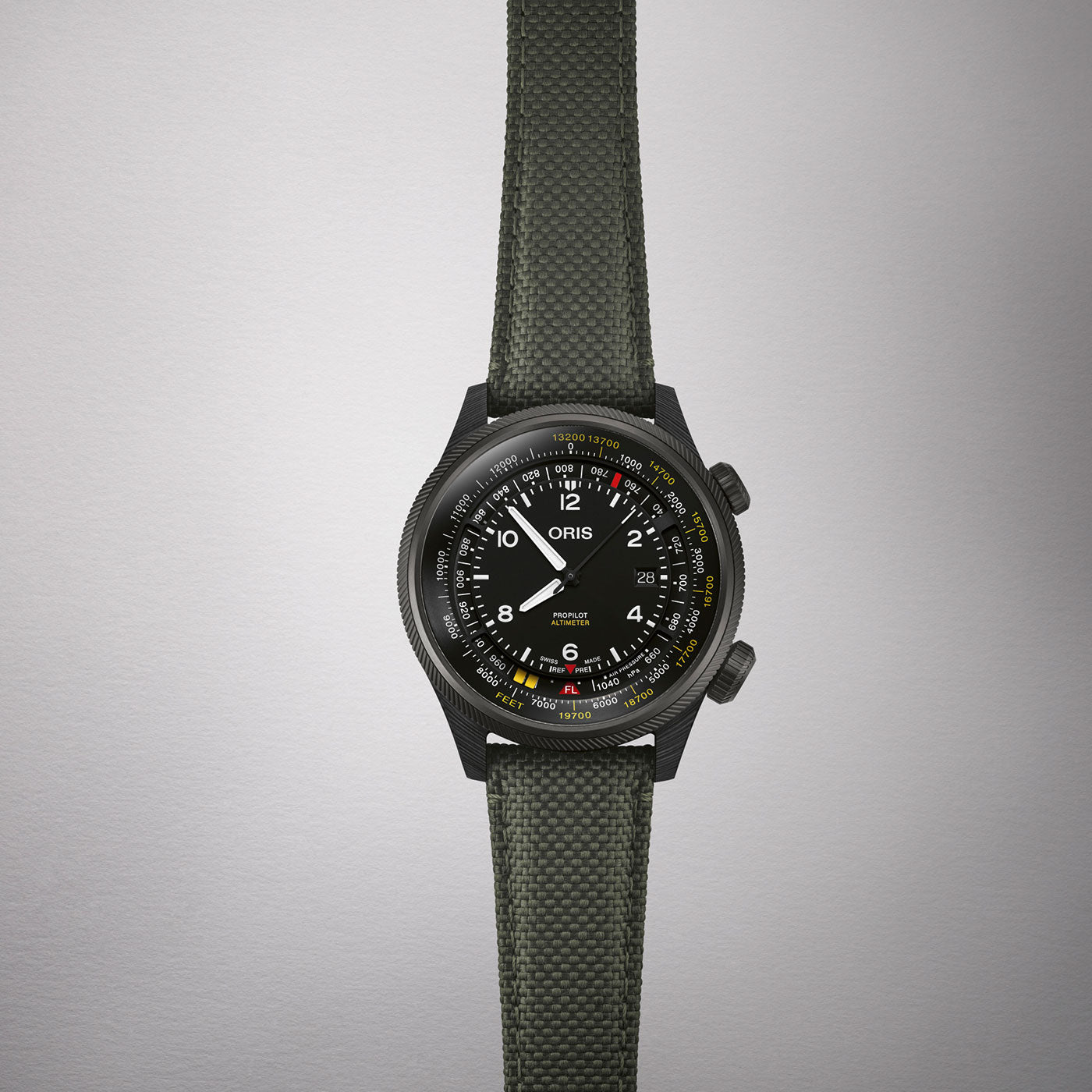 An Oris Propilot Altimeter Automatic 47mm watch by ORIS, featuring a black dial with white, yellow, and red numerals and markings. It includes a rotating bezel and comes with a green fabric strap. The background is a light, solid color.