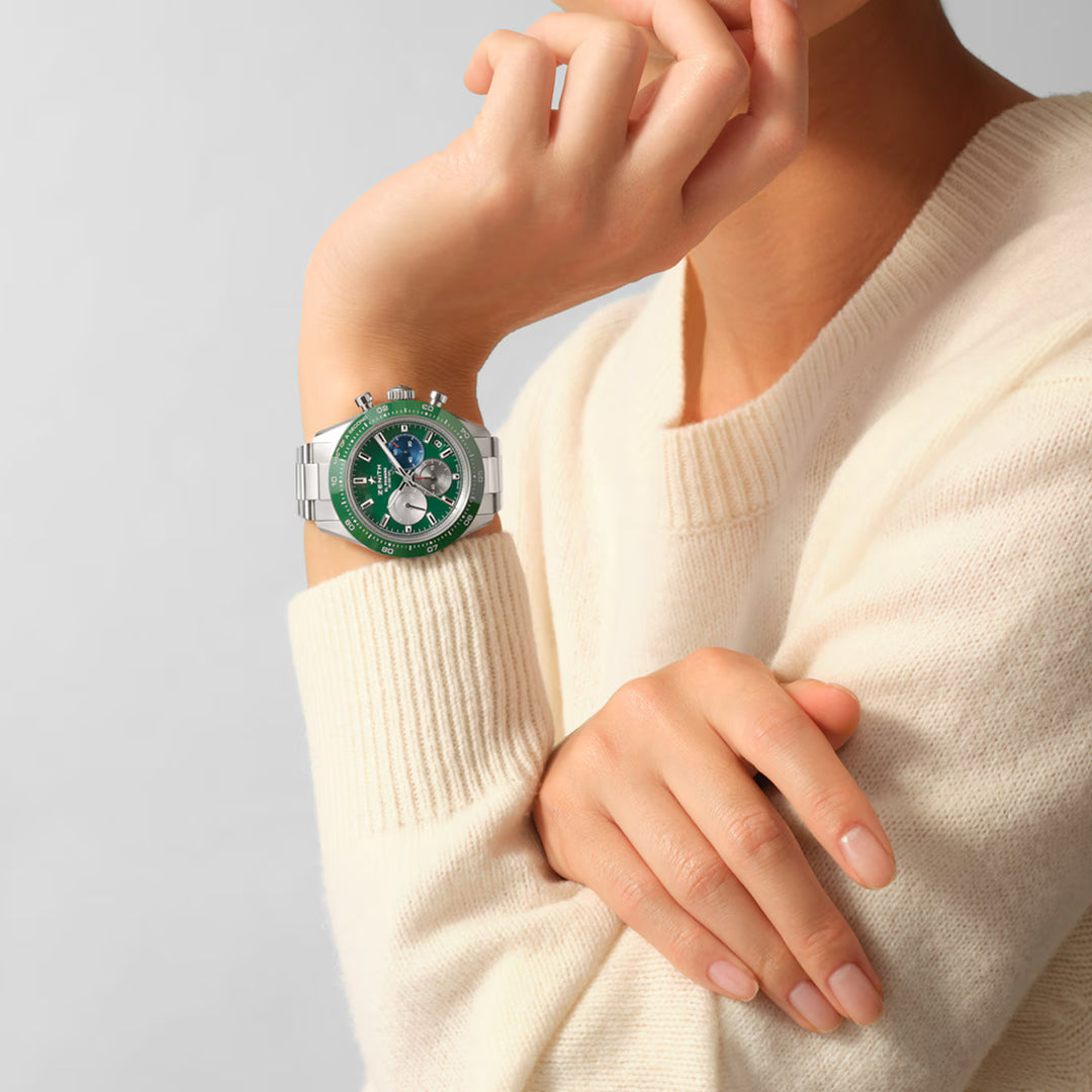 A person wearing a cream sweater elegantly showcases the Zenith Chronomaster Sport El Primero 3600 41mm. The wristwatch, with its stylish green dial and chronograph movement, catches attention as their elbow rests on a surface, highlighting both the watch and their graceful hand near the chin.