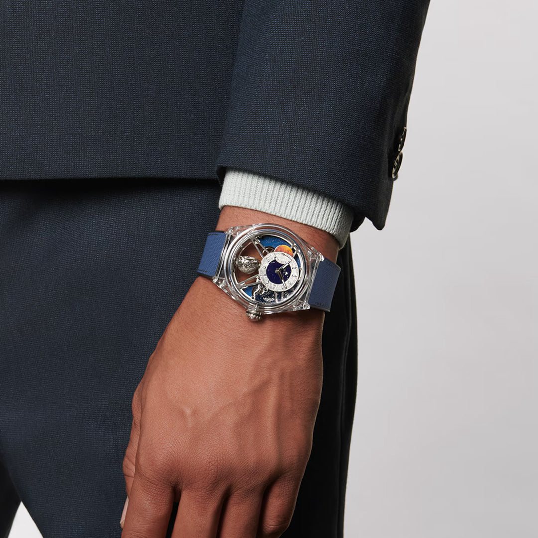 A person in a dark suit is shown from the waist down, highlighting their left hand and wrist with a ZENITH Defy Zero G El Primero 8812 S 46mm Watch. The transparent sapphire case showcases a detailed dial with gears and Gravity Control movement visible under the blue band.