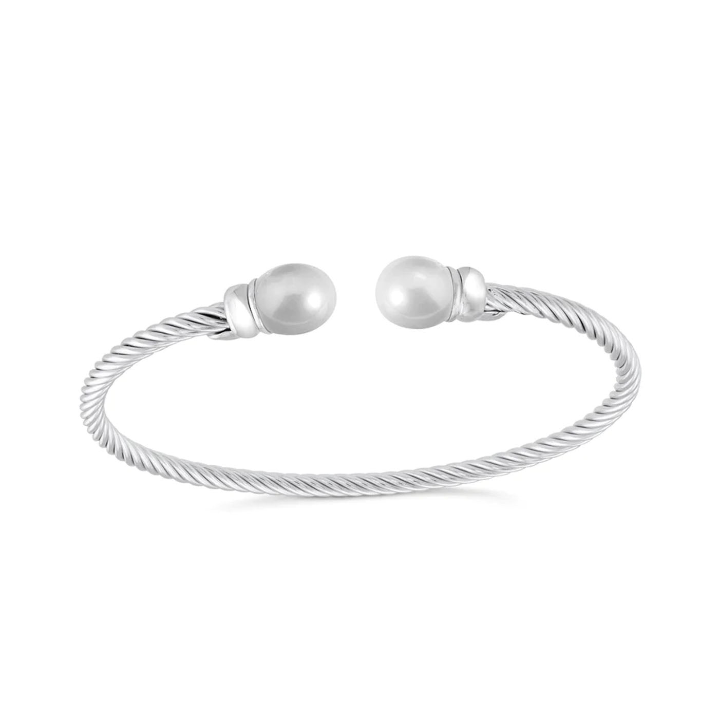 The Miss Mimi Twist Sterling Silver with Pearl Cuff Bracelet, from the renowned brand Miss Mimi by Yael, features a sleek and elegant design. This Italian-made bracelet showcases a twisted cable of sterling silver with open ends, each beautifully adorned with a freshwater pearl, highlighting the contrasting textures of metal and pearls against a plain white background.