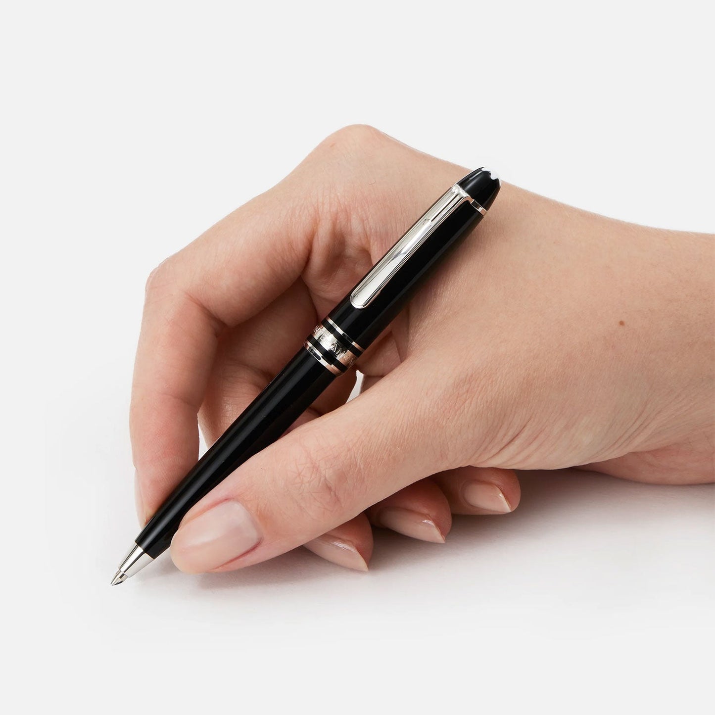 A hand holds a sleek Montblanc Meisterstück Platinum Coated Mozart Ballpoint Pen in black, poised to write on a white surface. The fingers are neatly manicured with natural polish, exuding an air of luxury writing.