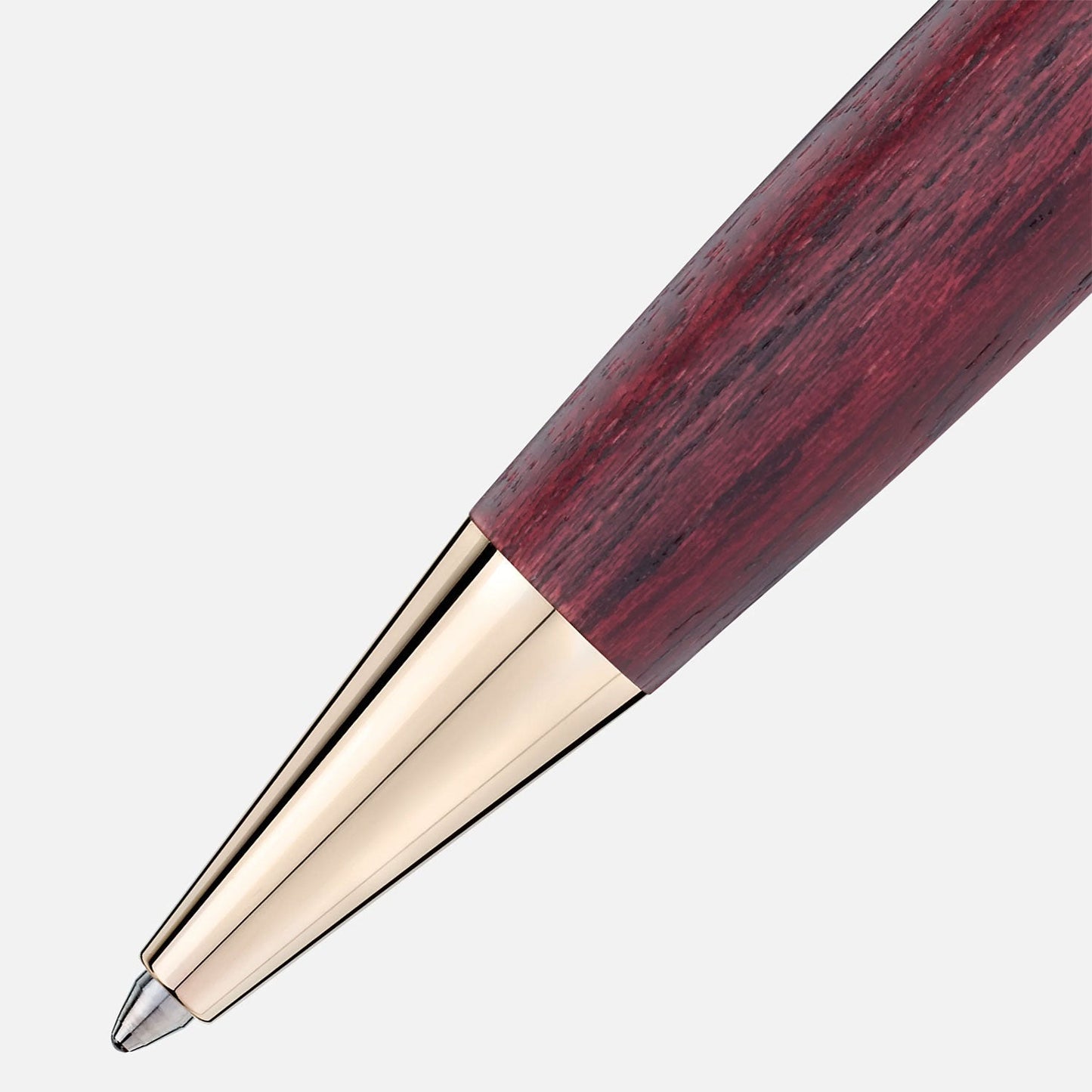 The close-up highlights the tip of a Montblanc Montblanc Meisterstück Le Petit Prince and Planet Classique Ballpoint Pen, which features a polished gold-colored metal nib and a wooden barrel with a rich, reddish-brown grain pattern. The background is light gray, perfectly accentuating the pen's elegant design.