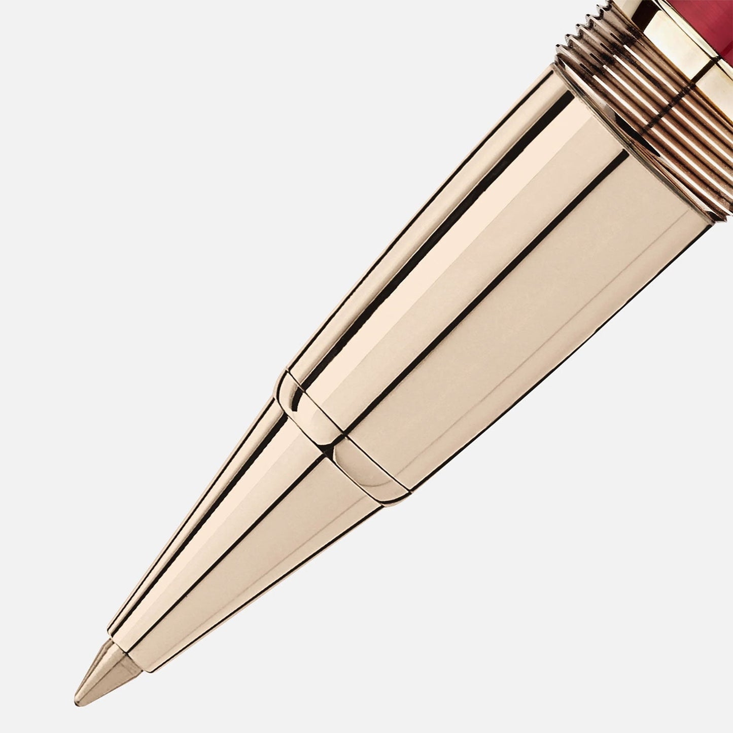 Close-up of a metallic pen tip with a sleek, shiny gold finish. The Montblanc Meisterstück Calligraphy Solitaire Burgundy Lacquer Rollerball Pen's body is angled diagonally, showcasing detailed grooves near the tip. The upper part features a rich burgundy lacquer design against a plain white background.