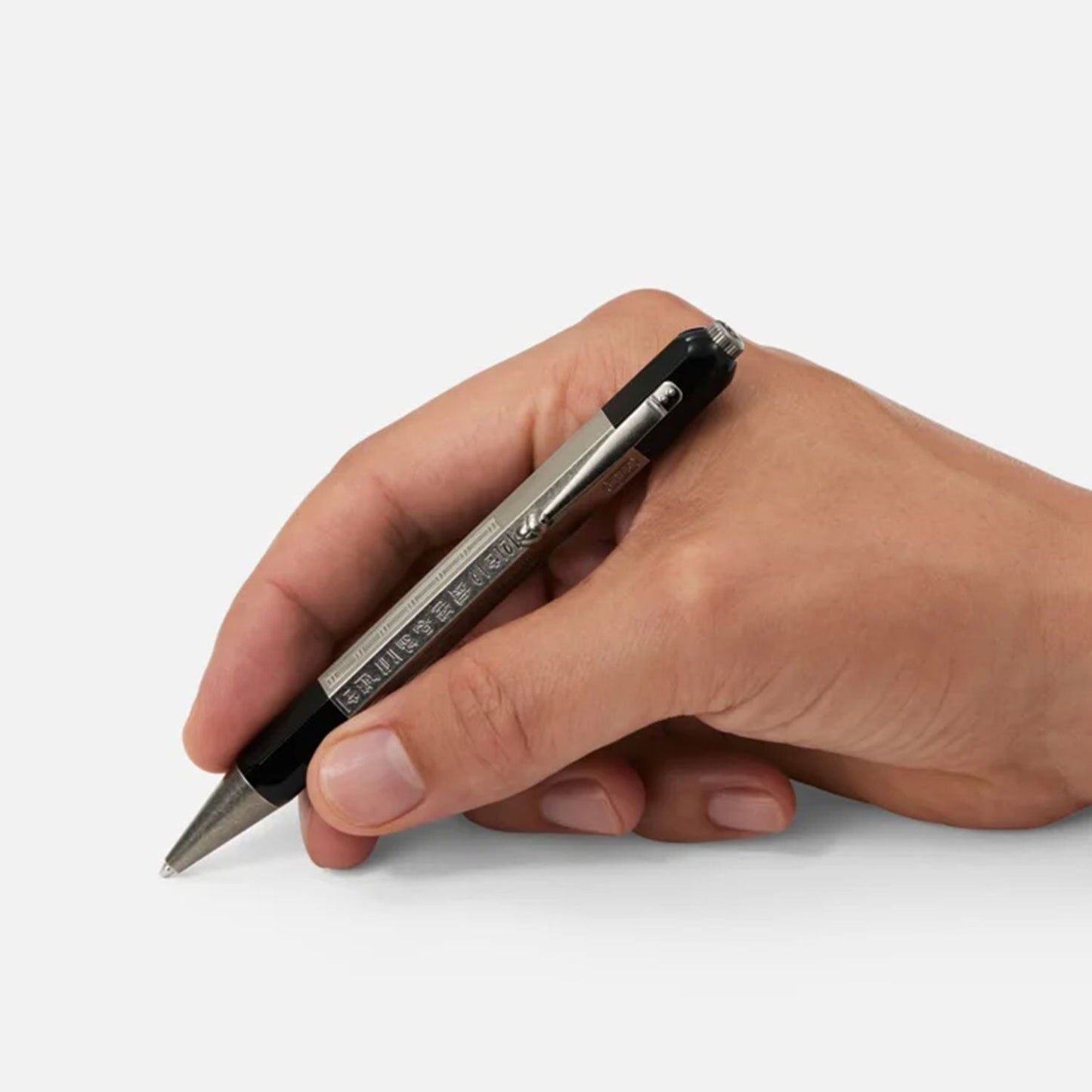 A hand holding a Montblanc Heritage Egyptomanian Doue Ballpoint Pen against a plain gray background, with fingers gently grasping it as if about to write.