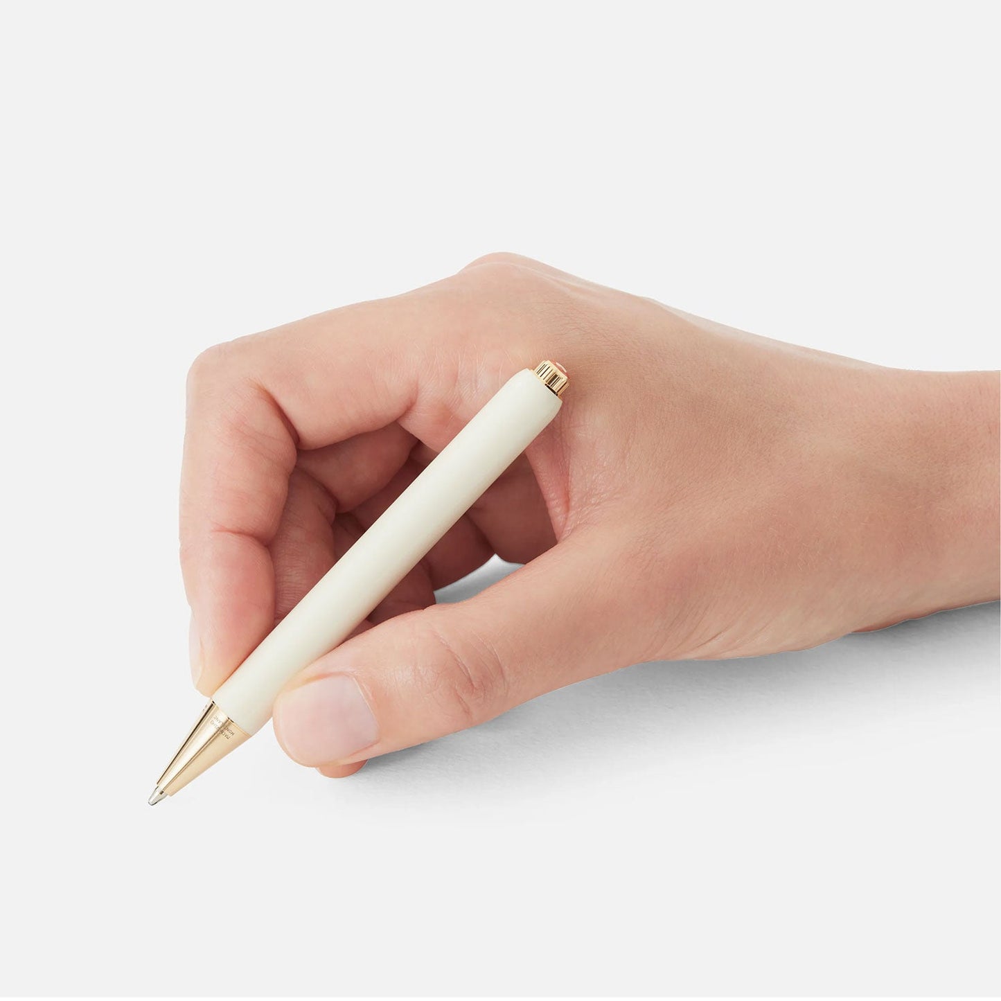 A hand holds an elegant Montblanc Heritage Rouge et Noir Baby Special Edition Ivory Coloured Rollerball Pen, featuring gold accents, poised against a white background. The pen is slightly tilted, with fingers gently grasping it, ready to write.