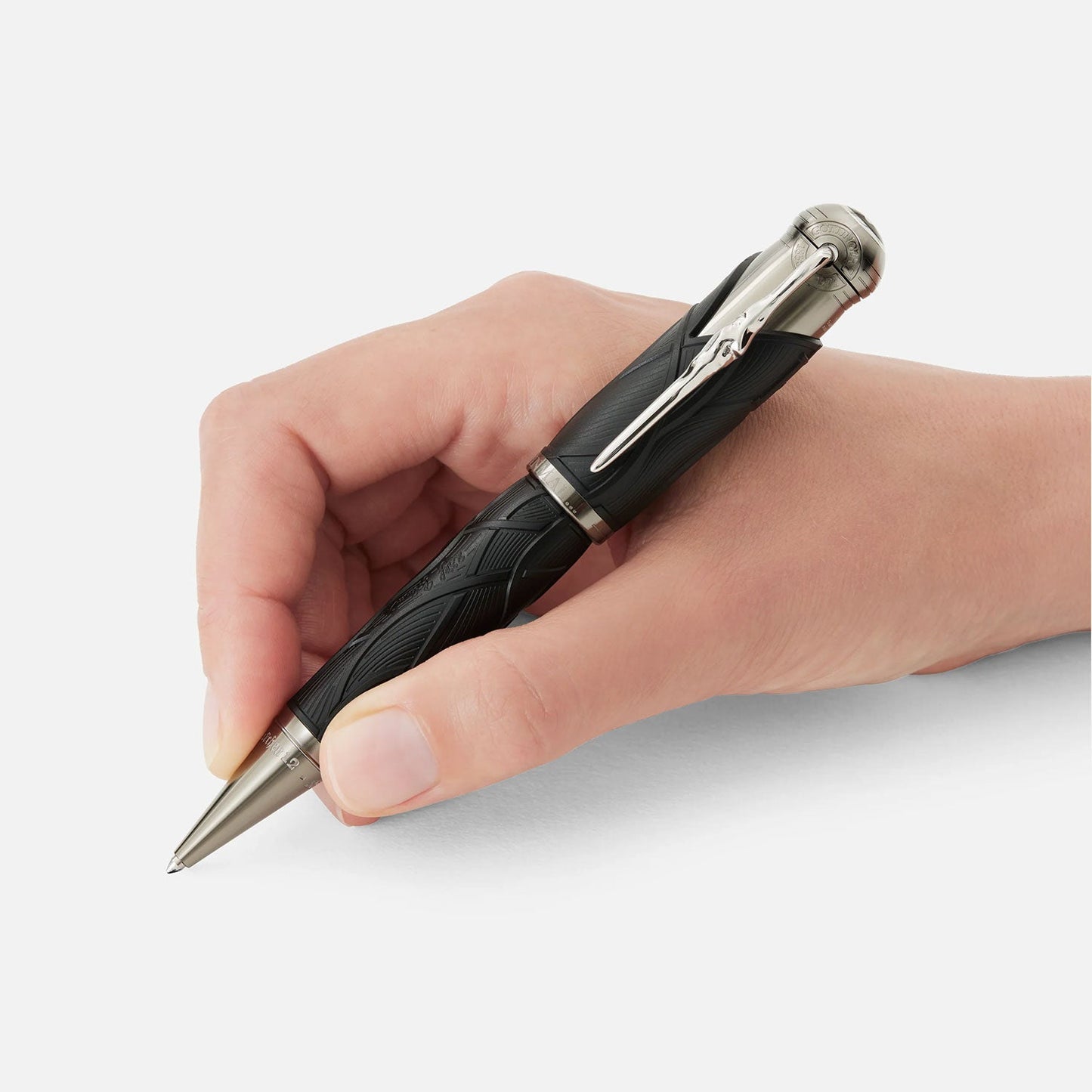 A hand holds an elegant black and silver pen against a plain white background, ready to write. The pen, the Montblanc Writers Edition Homage to the Brother Grimm Limited Edition Ballpoint Pen, features intricate patterns on the barrel and a metallic clip on the cap.