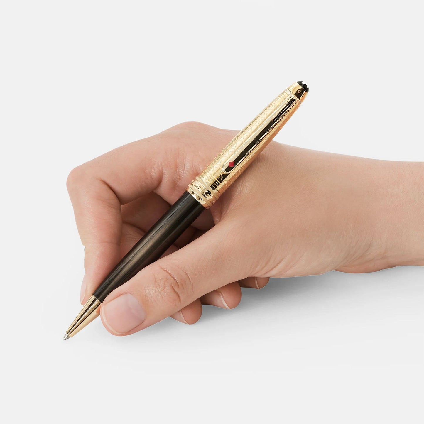 A hand holds the luxurious Montblanc Meisterstuck Around the World in 80 Days Doué Classique Ballpoint Pen, showcasing a gold and black design with intricate engravings on the cap and a shiny gold clip. This pen, inspired by Jules Verne's adventurous tales, is set against a neutral white background.