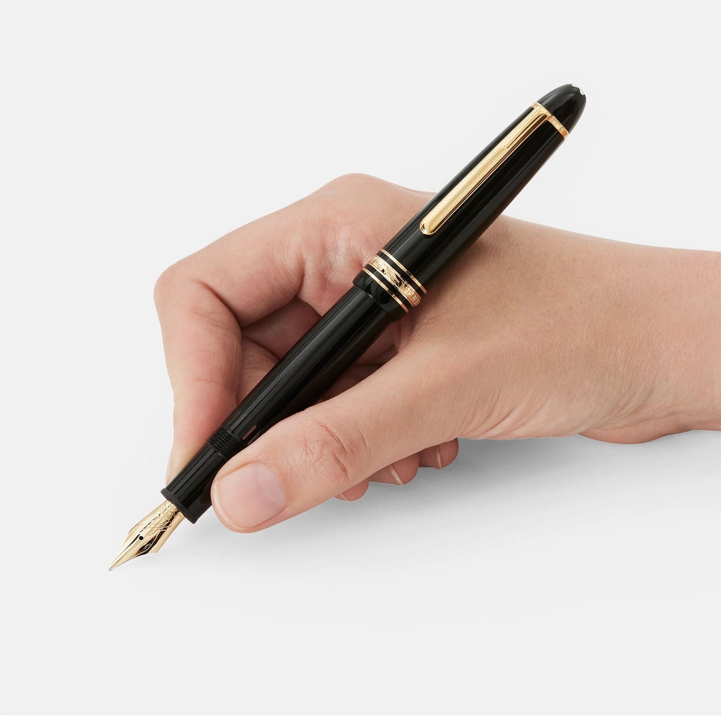 A hand holding a Montblanc Meisterstück Le Grand Calligraphy Flexible Nib Fountain Pen is poised above a white surface, ready to write. The Montblanc pen's luxury design and its flexible nib are highlighted against the plain background.