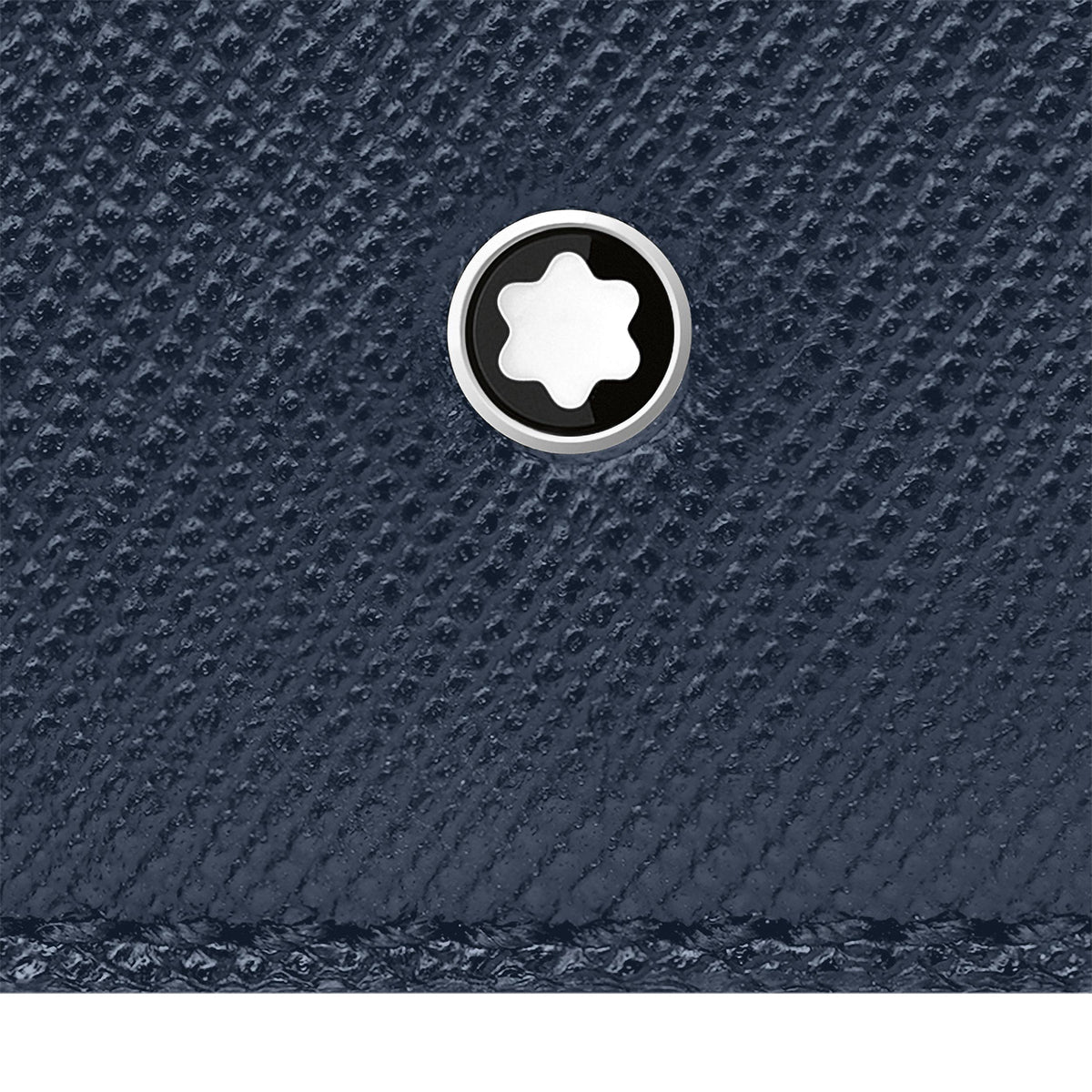 Close-up of a textured dark blue surface with a round, silver emblem featuring a star design at the center, reminiscent of the elegant finish of the Montblanc Sartorial Leather Business Card Holder.