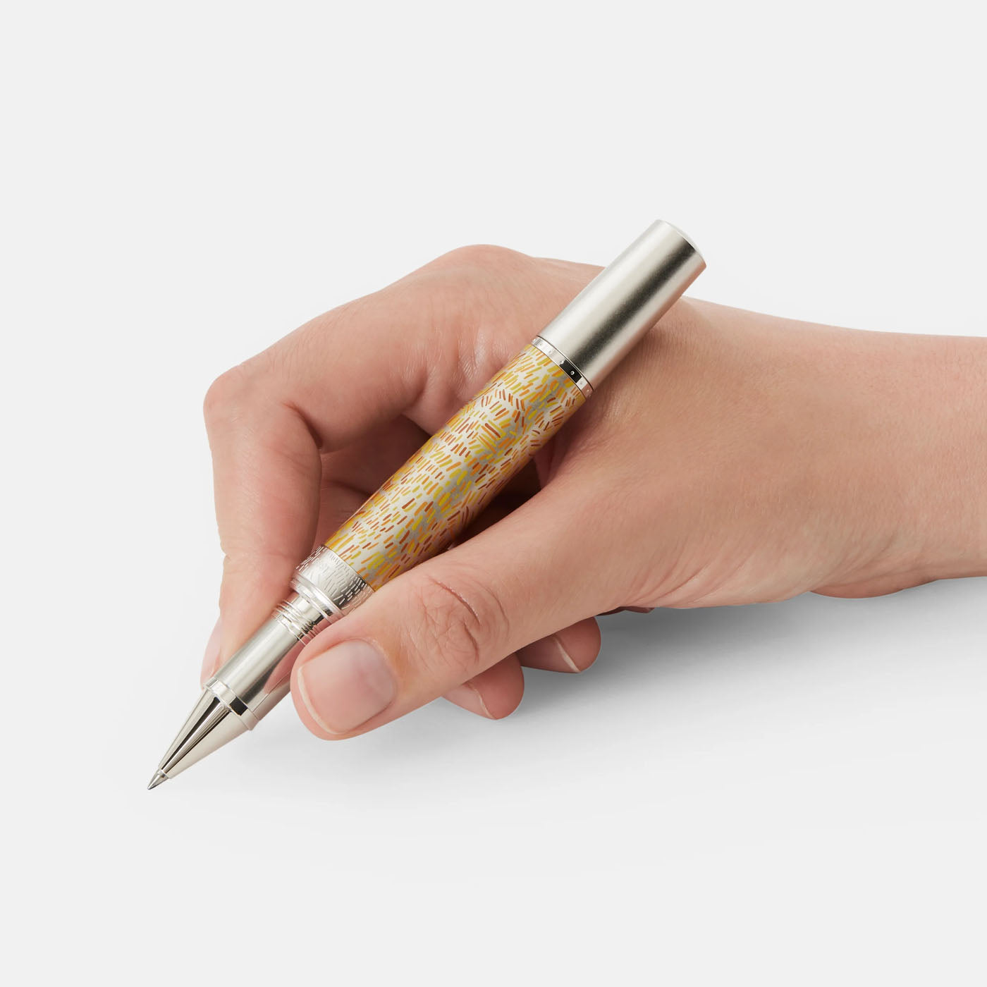 A hand holds a Montblanc Masters of Art Homage to Vincent Van Gogh Limited Edition 4810 Rollerball Pen, featuring a patterned barrel and metallic cap. This exquisite limited edition piece captures the vibrant essence of Van Gogh’s Provencal wheatfields against a crisp white background, ready to inspire creativity.