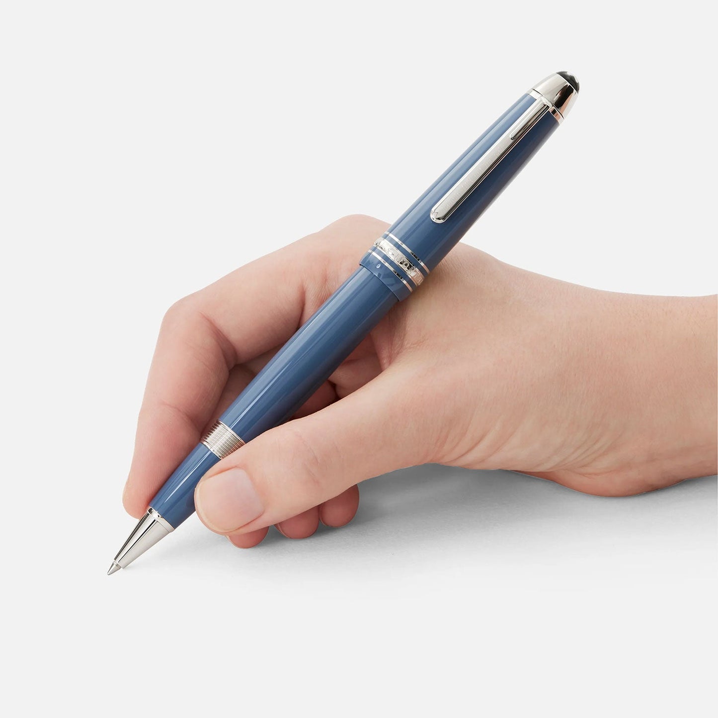 A hand holding a Montblanc Meisterstück Glacier LeGrand Blue Rollerball Pen, poised to write on a blank surface. The pen's blue-gray precious resin beautifully complements the plain white background.