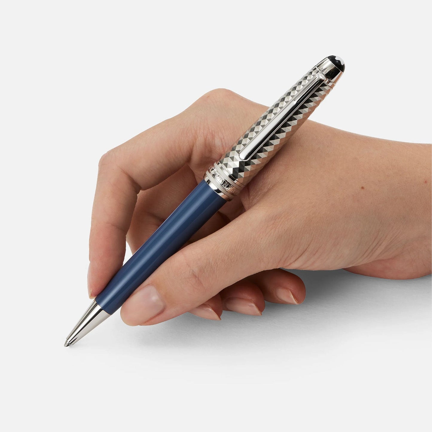 A hand holds the Montblanc Meisterstück Glacier Doué ballpoint pen, showcasing a sophisticated design with its sleek blue-colored precious resin barrel and platinum-coated metal cap. The pen also features a textured silver grip and a shiny finish, all set against a plain white background.