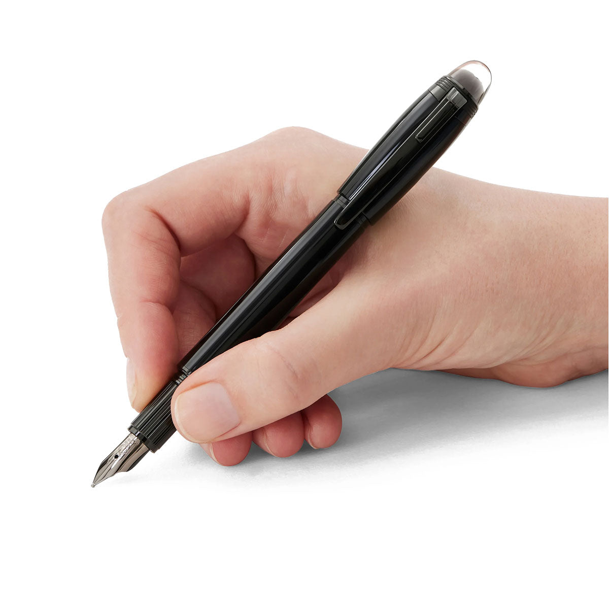 A hand holds a Montblanc Starwalker Black Cosmos Precious Resin Fountain Pen, poised to write on a blank white surface. Reflecting the theme of space exploration, the pen features a metallic tip and glossy finish.