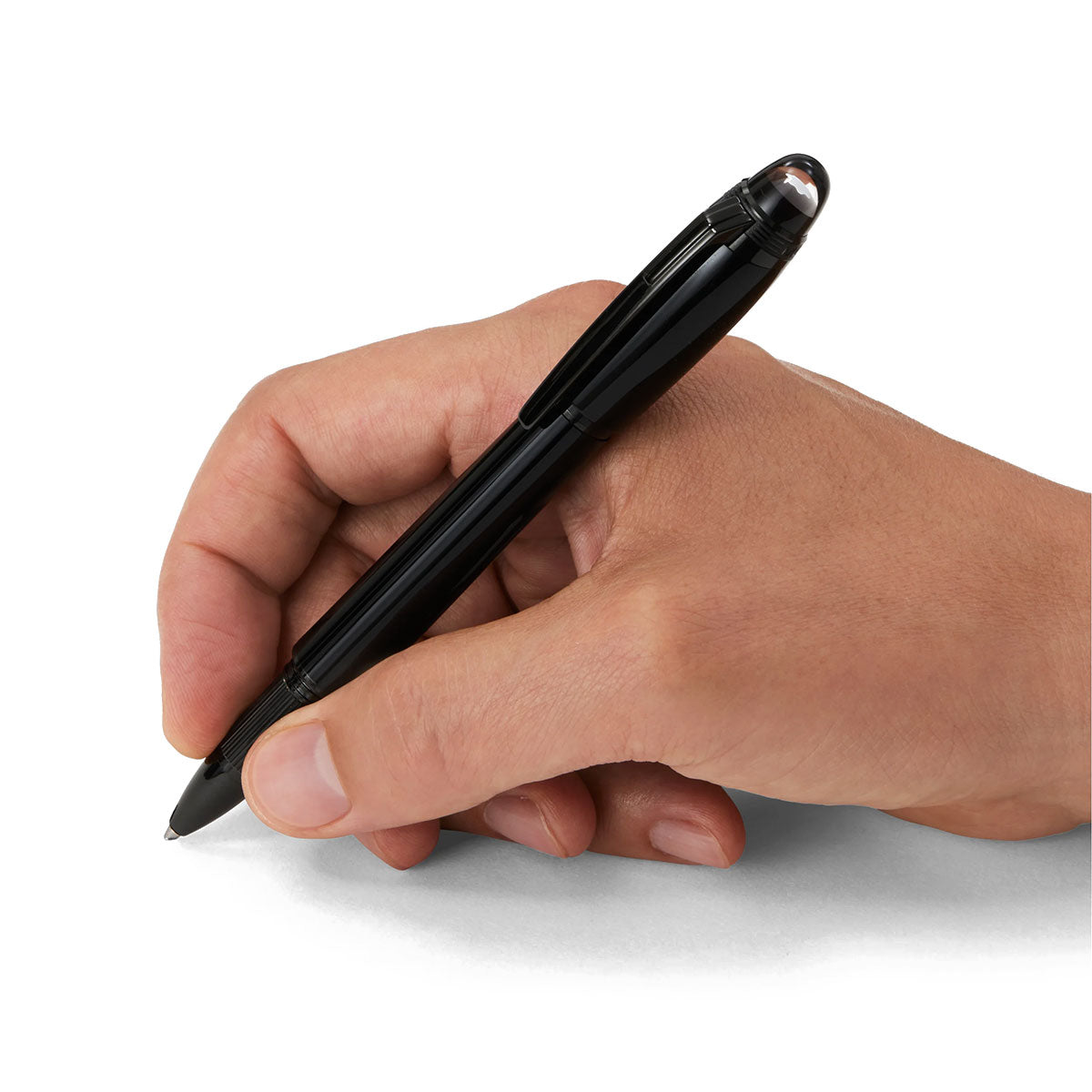 A hand grips the sleek, glossy Montblanc Starwalker Black Cosmos Precious Resin Ballpoint Pen poised to write on a white surface. The fingers hold it gently, anticipating the next words or strokes. The pen's silver clip catches the light against the plain, bright background.