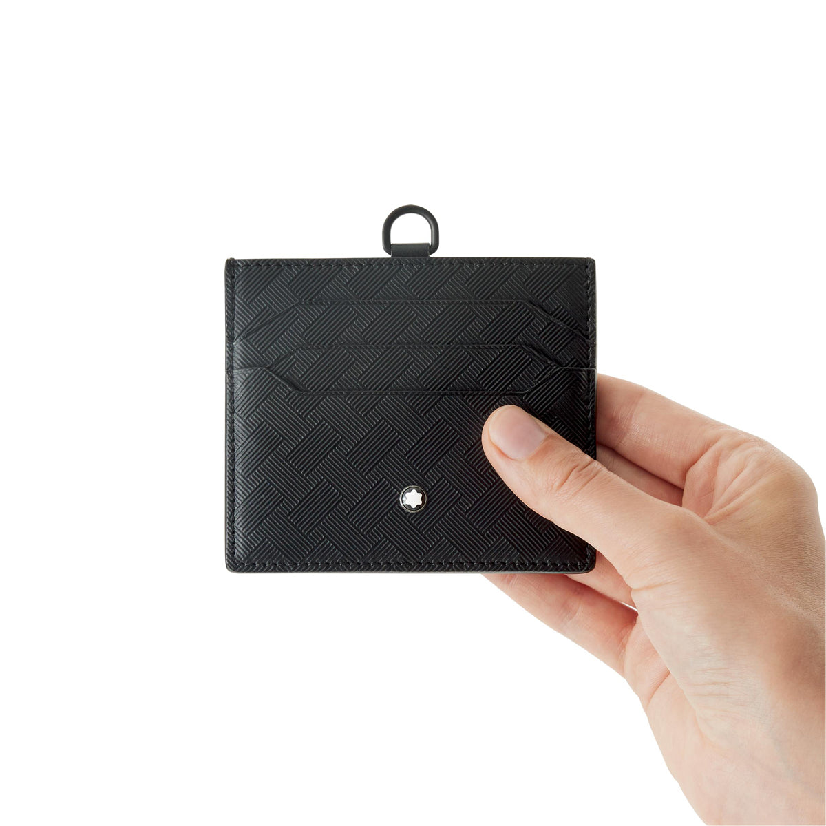 A hand holds a Montblanc Extreme 3.0 Leather Card Holder 6cc with a textured grid pattern against a white background. The card holder features a small metallic logo on the front and a loop at the top. Only the hand and card holder are visible.