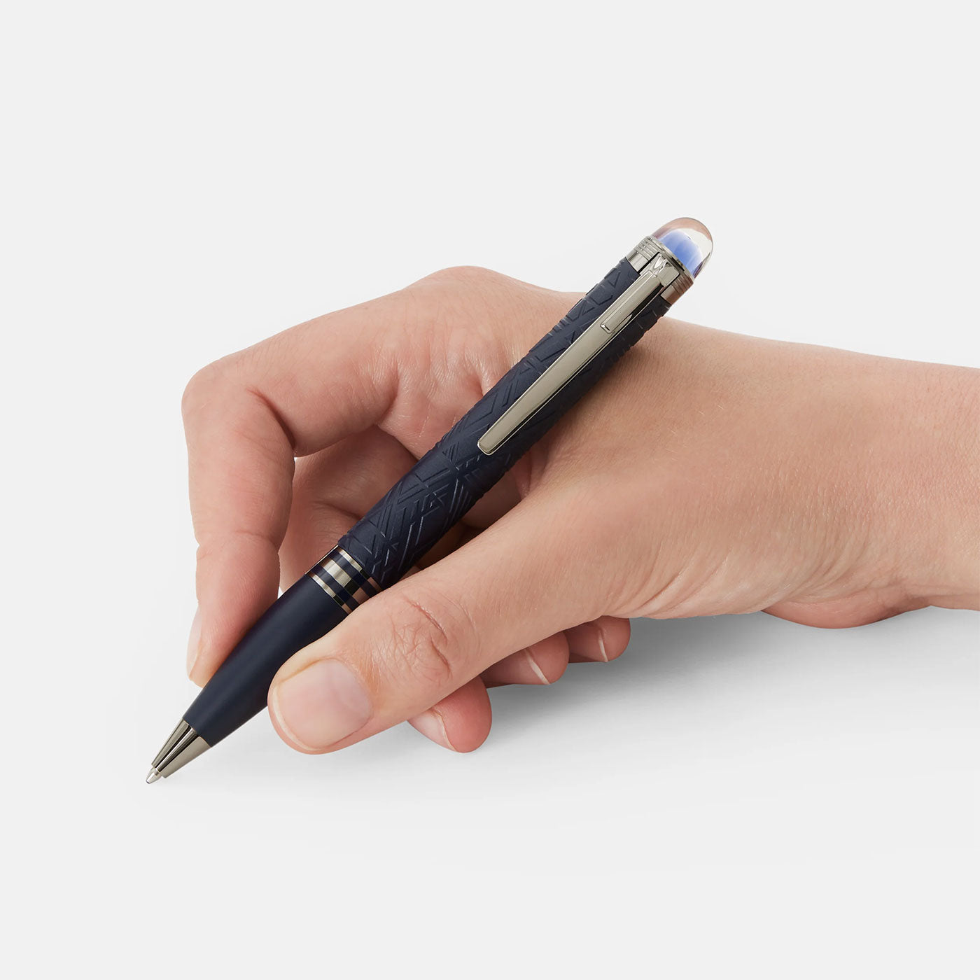 A Montblanc Starwalker SpaceBlue Resin Ballpoint Pen with silver accents is held against a plain white background. The pen features intricate designs reminiscent of the Widmanstätten Pattern on the barrel and boasts a shiny clip.