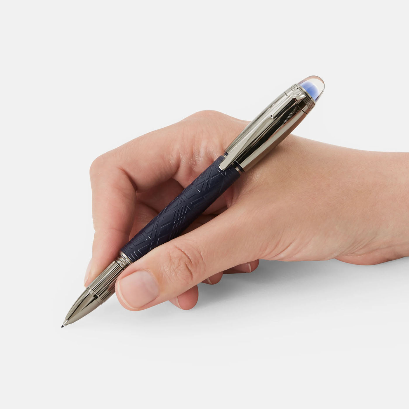 A hand holds the elegant Montblanc Starwalker SpaceBlue Resin Doue Fineliner Pen, characterized by its sleek dark blue finish with silver accents and the iconic Montblanc emblem, poised above a white surface. The pen boasts a detailed design reminiscent of the Widmanstätten Pattern, featuring a reflective tip.