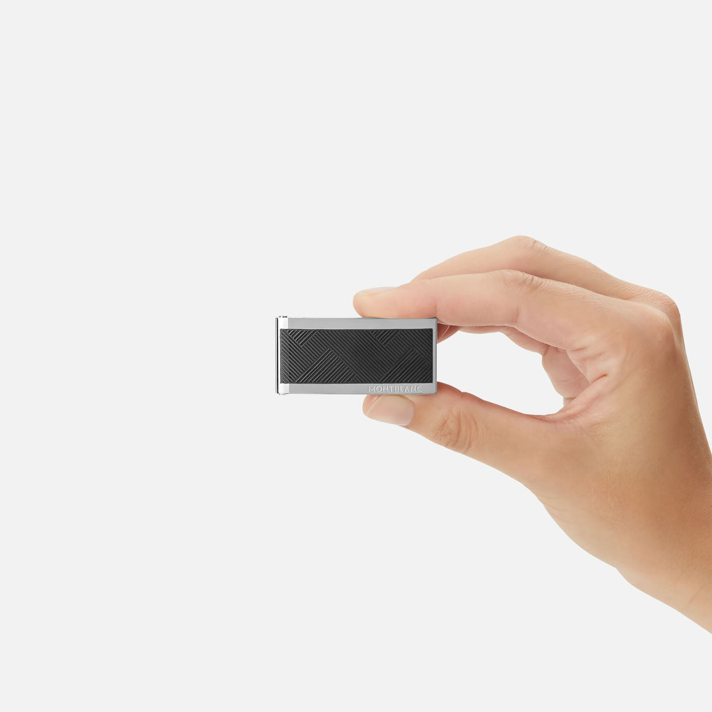 A hand holding a small rectangular device with a textured black surface is set against a plain white background, showcasing the sleek style of the Montblanc Extreme 3.0 Collection Money Clip with subtly integrated stainless steel accents.