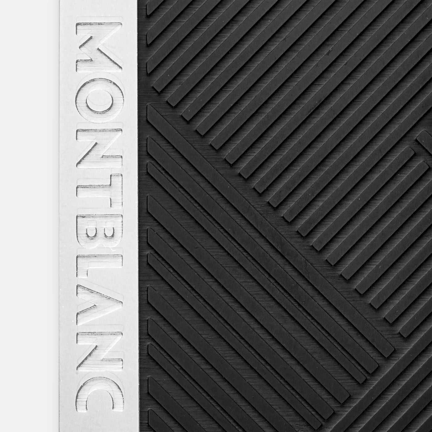 A detailed view of a textured black surface shows diagonal lines creating geometric patterns. To the left, a vertical silver strip features the text "MONTBLANC." This design exudes a modern and sophisticated aesthetic, showcasing the Montblanc Extreme 3.0 Collection Money Clip from Montblanc.