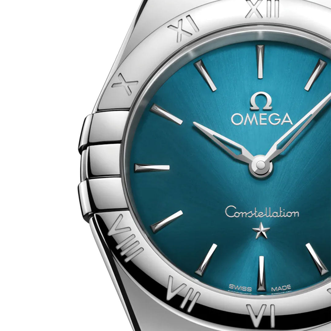 Close-up of the OMEGA Constellation Quartz 28mm Watch featuring a peacock blue dial, silver hands, Roman numeral bezel, polished stainless steel case, and visible OMEGA logo with "Constellation" on the dial.