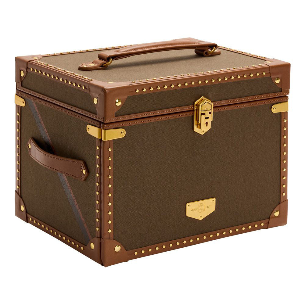 The WOLF 1834 Ida Trunk Jewellery Box, by the brand WOLF, is a vintage-style olive green and brown leather trunk adorned with brass stud detailing and gold accents. It features a custom-designed lock, top handle, side handle, and gold latch. With leather corner protectors and an emblem-adorned gold plate, it embodies timeless elegance.