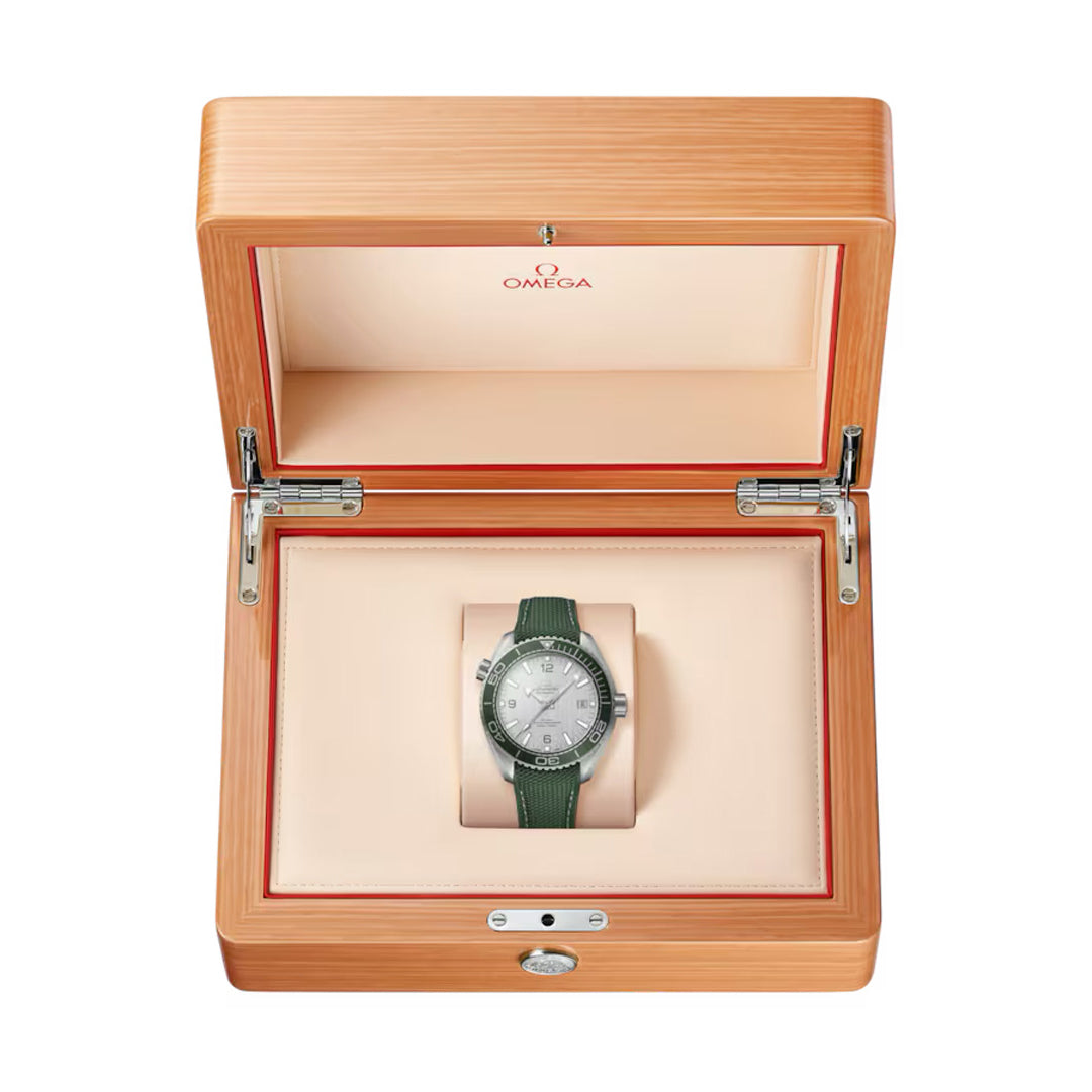 An OMEGA Seamaster Planet Ocean 600M Co-Axial Master Chronometer 43.5mm watch is beautifully showcased in an open wooden box with a beige interior. The lid displays the red OMEGA logo. This dive watch features a green strap and metal case, set against a plain white background.