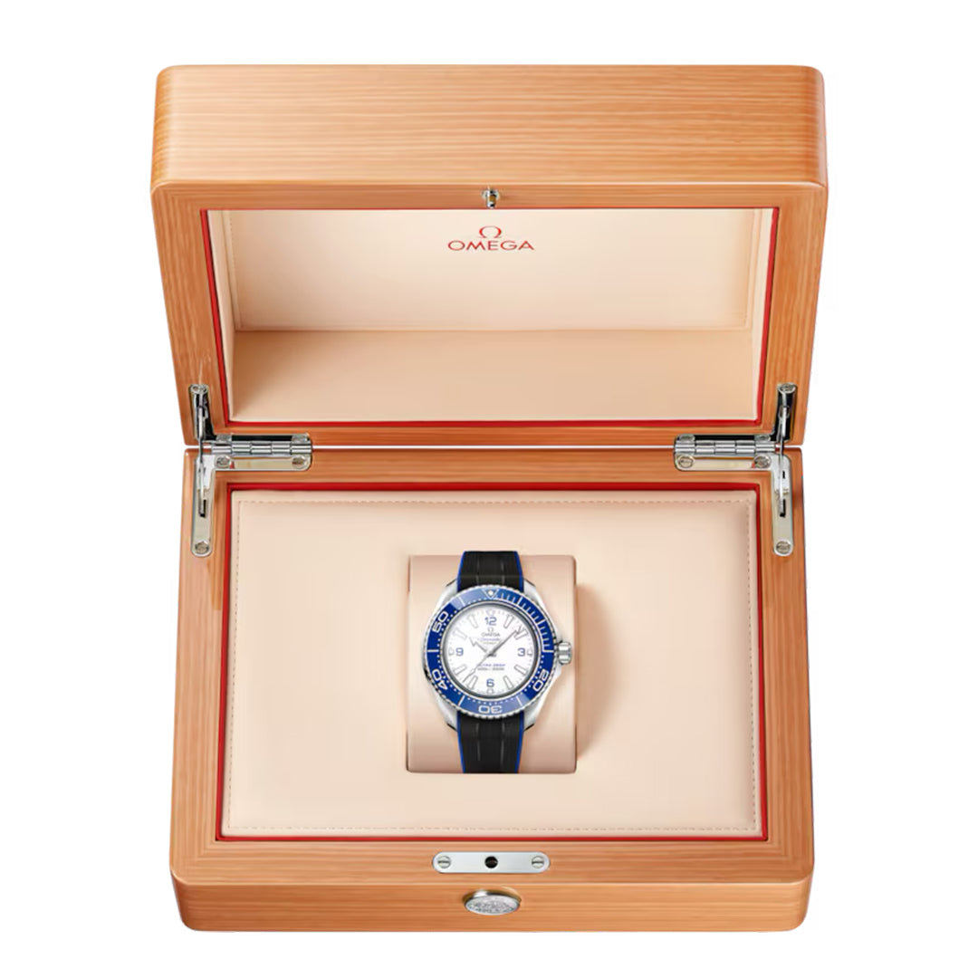 The OMEGA Seamaster Planet Ocean 6000M Ultra Deep Co-Axial Master Chronometer 45.5mm watch, featuring a blue bezel and black strap, is showcased in a wooden box with a beige interior. Known for its water resistance, it blends elegance and durability for adventurous saturation divers.