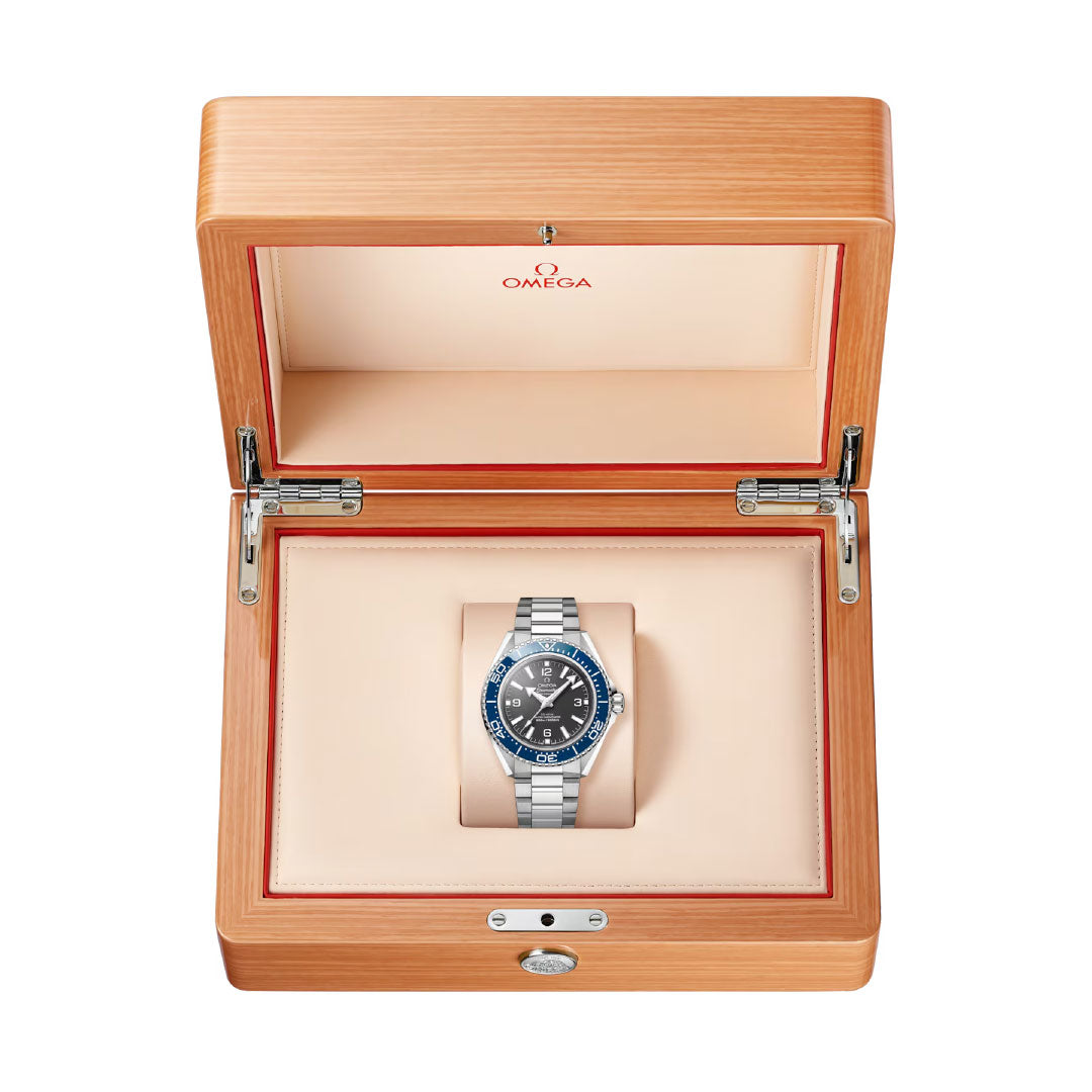 A silver OMEGA Seamaster Planet Ocean 600M Co-Axial Master Chronometer 42mm Watch with a blue bezel and dark face sits in an open light wood box lined with cream padding, the Omega logo visible inside the lid.