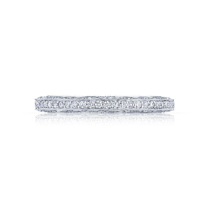 A detailed Tacori Classic Crescent 18K white gold band with intricate engravings and round brilliant pavé-set diamonds encircling it, showcased against a white background with a subtle reflection beneath.