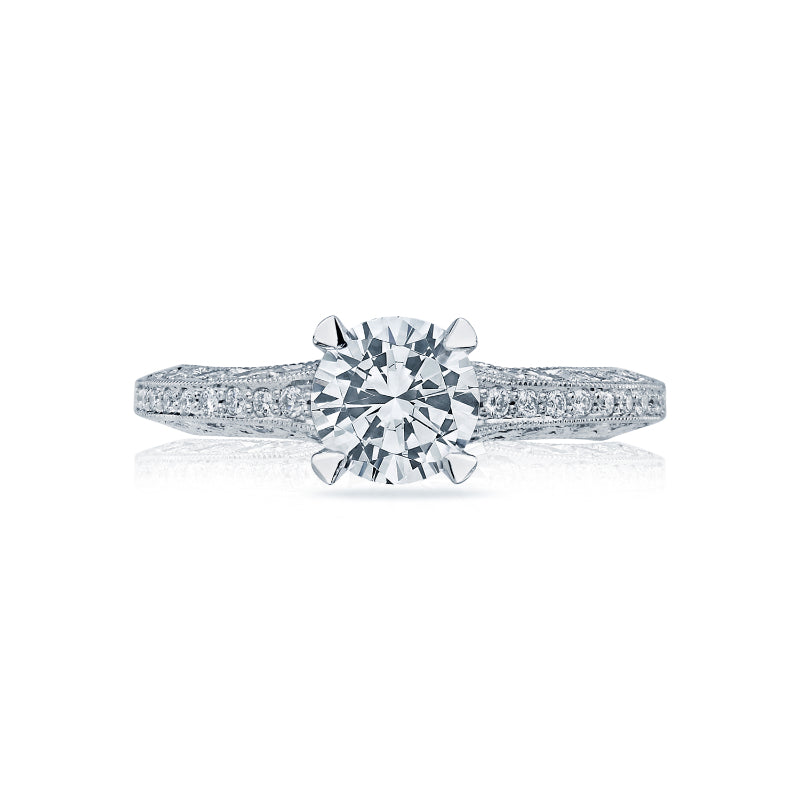 The Tacori Classic Crescent 18K White Gold Engagement Ring prominently features a round, brilliant-cut diamond centerpiece, crafted by expert gemologists at Tacori. The ring is set on a meticulously detailed band adorned with small, sparkling stones that enhance its elegance and shine.