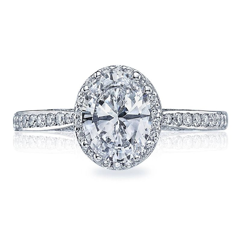 The Tacori Dantela 18K White Gold Oval Semi Mount Engagement Ring showcases a stunning large oval solitaire diamond at its center, surrounded by a hidden halo of smaller diamonds. The band glistens with an array of tiny diamonds, making it an elegant choice for anyone seeking a sophisticated engagement ring from Tacori.