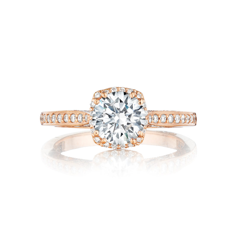 The Tacori Dantela engagement ring in 18K rose gold features a round brilliant center accented by a hidden halo of smaller diamonds. Its band, adorned with additional diamonds, offers an elegant and sparkling design.