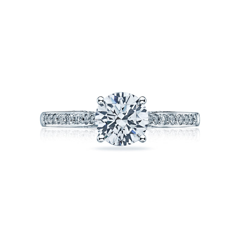 Introducing the Tacori Dantela 18K White Gold Round Brilliant Semi Mount Solitaire Engagement Ring with Diamond Band, a masterpiece of elegance and craftsmanship. This exquisite piece features a stunning round-cut diamond at its center, surrounded by smaller round-brilliant diamonds encrusted along the band. Set against a white background, this ring epitomizes timeless beauty and is expertly crafted by Tacori gemologists.