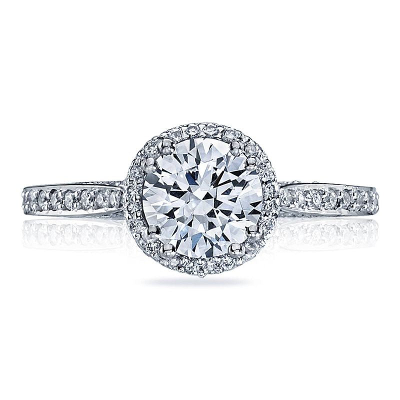 The Tacori Dantela Platinum Round Brilliant Semi Mount with Diamond Band and Halo Engagement Ring features a central round diamond surrounded by a halo of smaller diamonds. Its Cathedral foundation band is adorned with additional diamonds, exuding an elegant and sparkling charm.